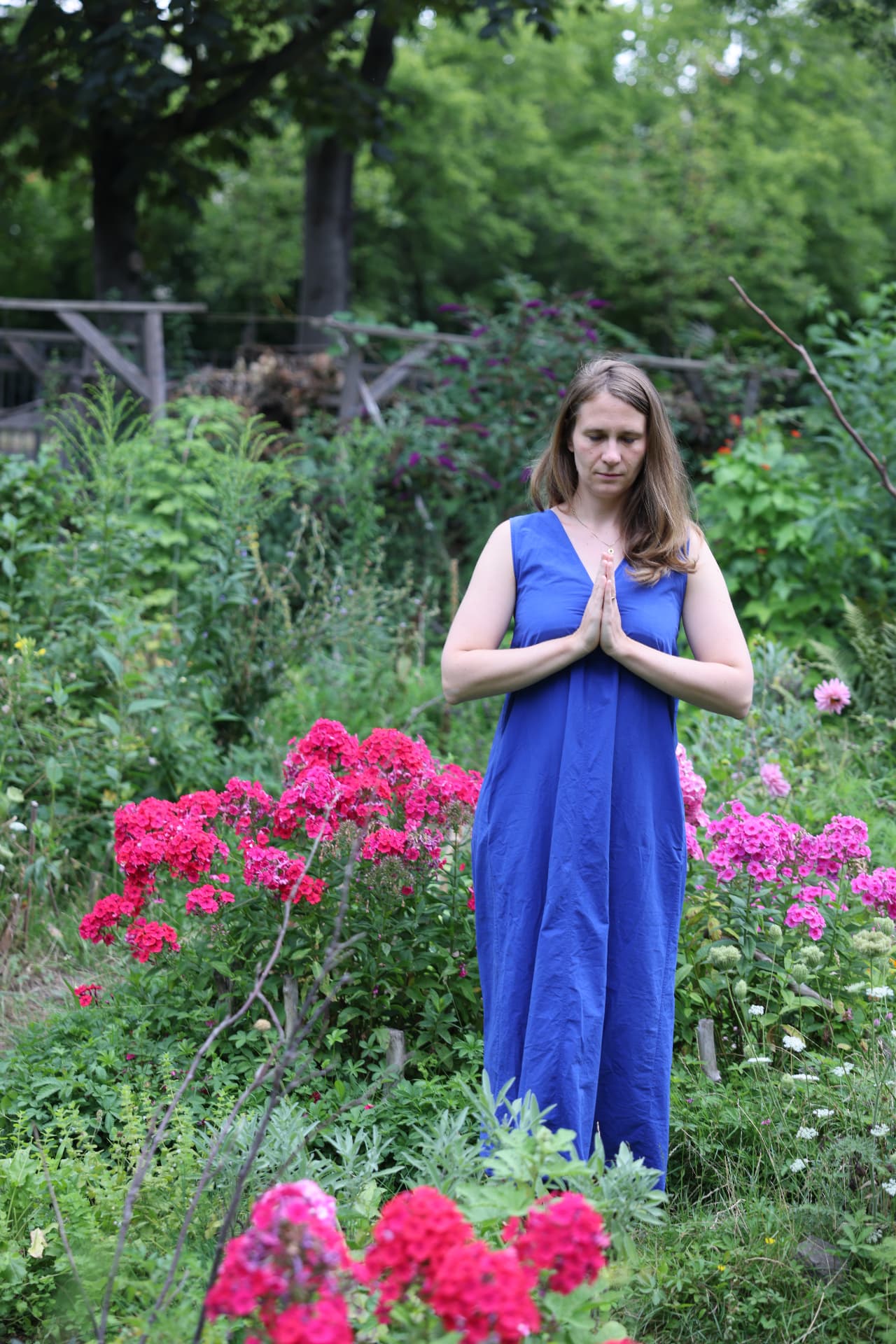 Marie in a blue dress standing in a garden with hands at heart center